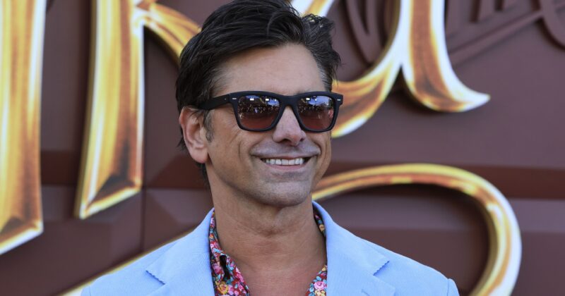 First Images of Lizzy Caplan & John Stamos’ Offbeat Robbery Comedy Thriller ‘Drag’ Unveiled