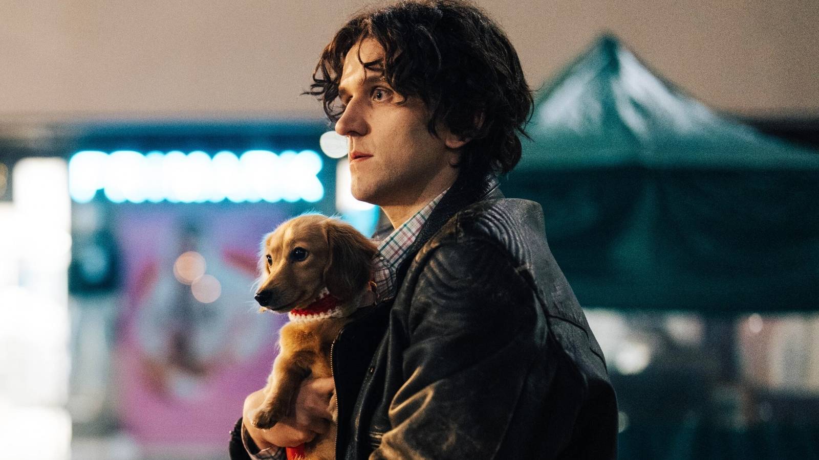 Harry Melling sosteniendo un perro en la película Pillion